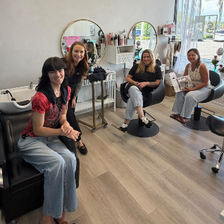 Four women smiling together in a salon suite